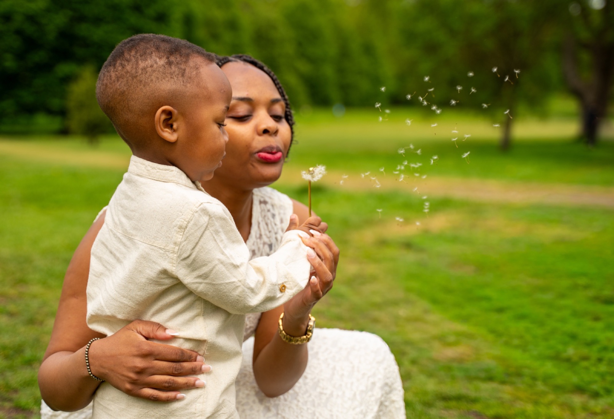 Mother and young son blowing a dandelion together in a Buckinghamshire park